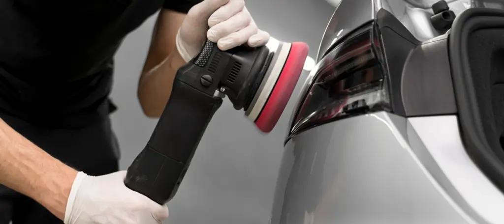 Professionele autodetailer die een achterlicht polijst met een elektrische polijstmachine om de glans en helderheid te herstellen.